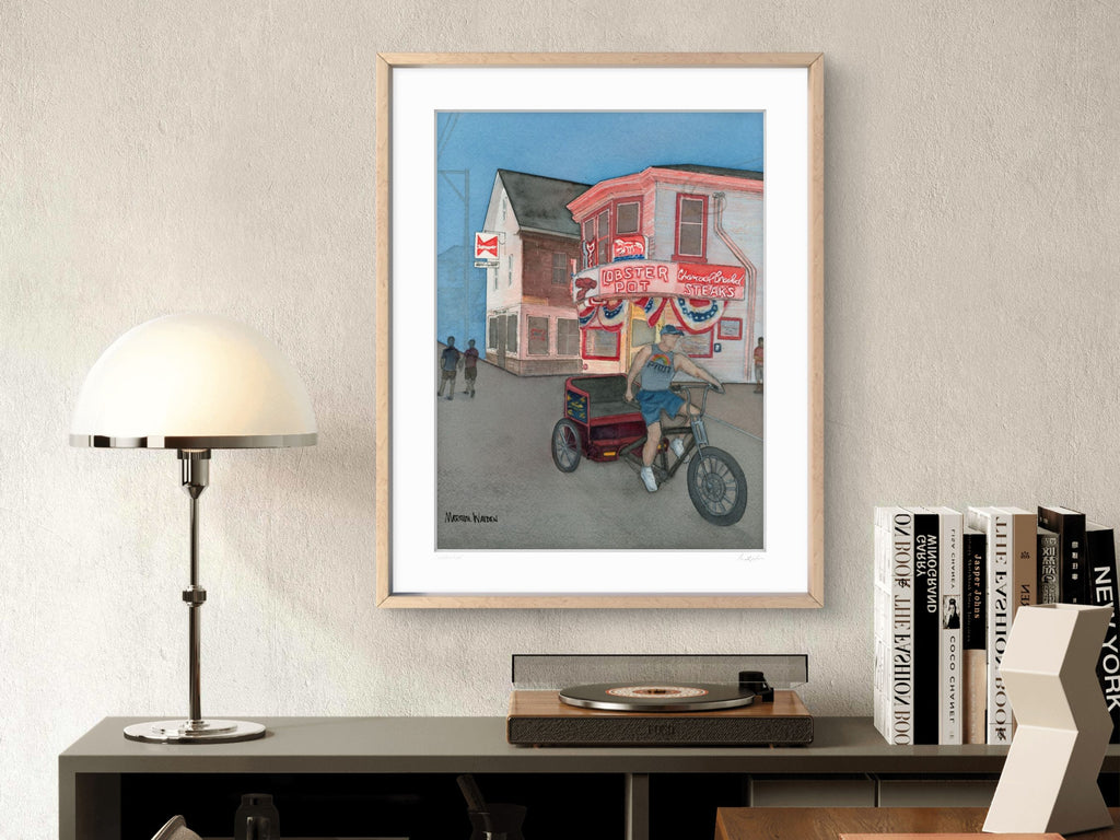 A lifestyle photograph of a maple framed watercolor print above a bookshelf titled "Catch A Ride" signed by artist Marshal Walden