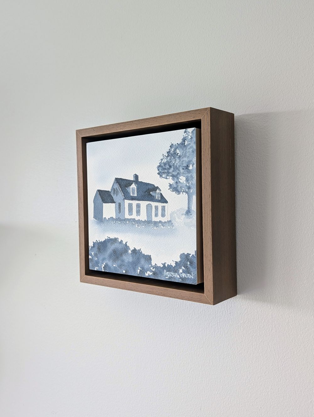 Right side view of Abide, a minimalist monochrome watercolor study of a coastal home, isolated within a deep light walnut float mount frame on a neutral wall.