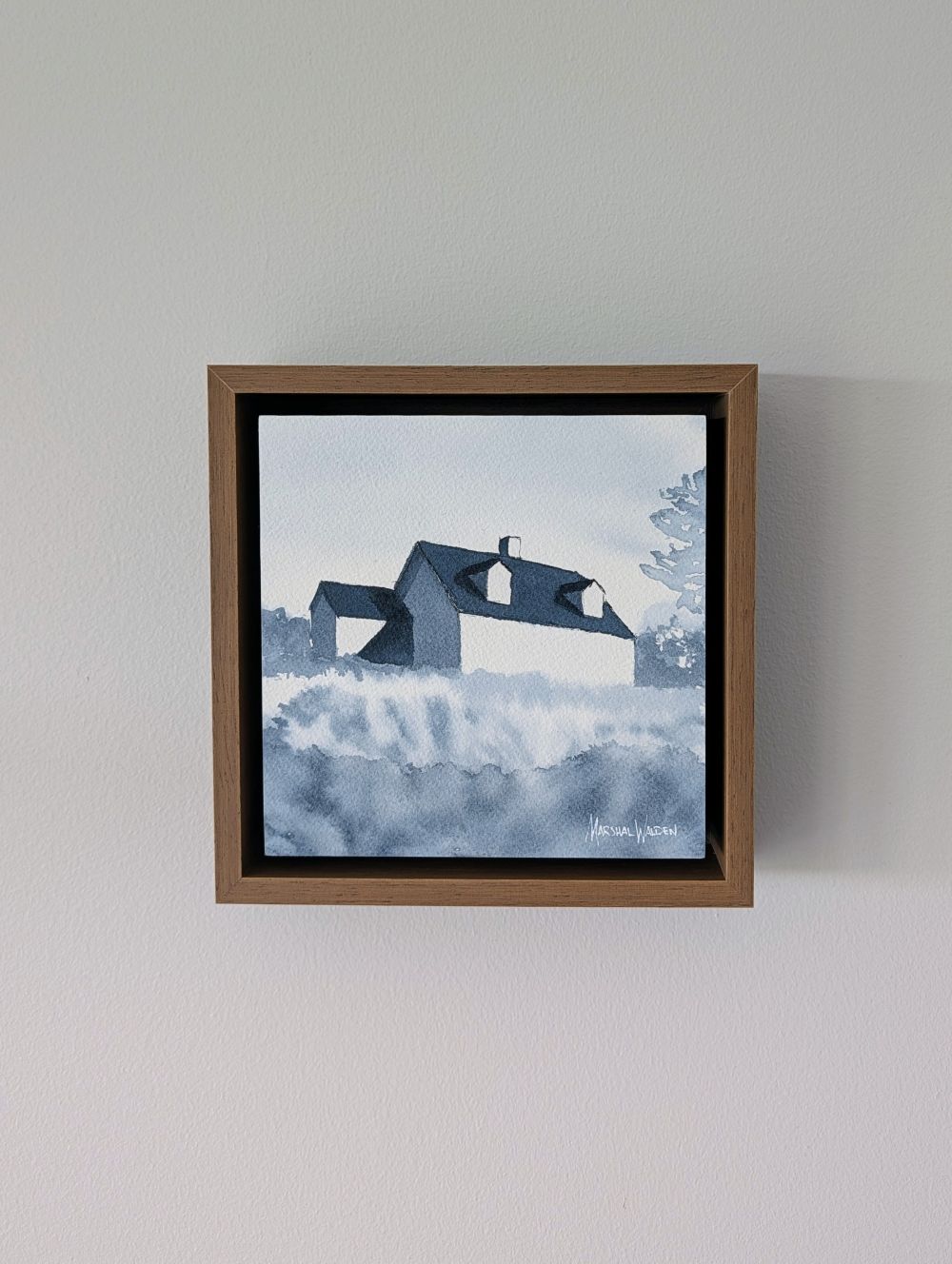 Front view of Emergence, a minimalist monochrome watercolor study of a coastal home, isolated within a deep light walnut float mount frame on a neutral wall.