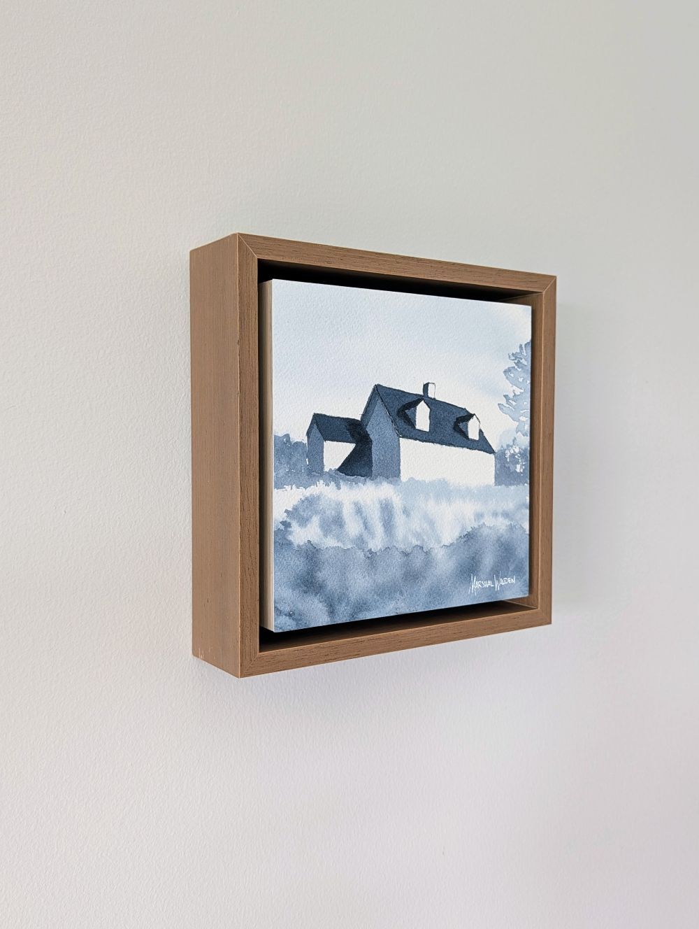 Left side view of Emergence, a minimalist monochrome watercolor study of a coastal home, isolated within a deep light walnut float mount frame on a neutral wall.