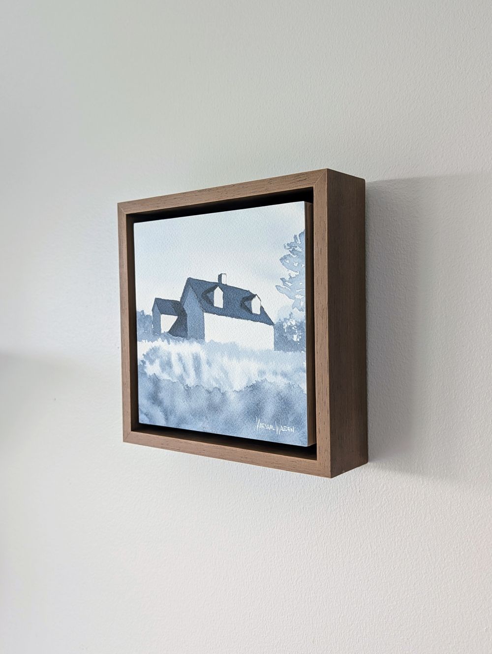Right side view of Emergence, a minimalist monochrome watercolor study of a coastal home, isolated within a deep light walnut float mount frame on a neutral wall.