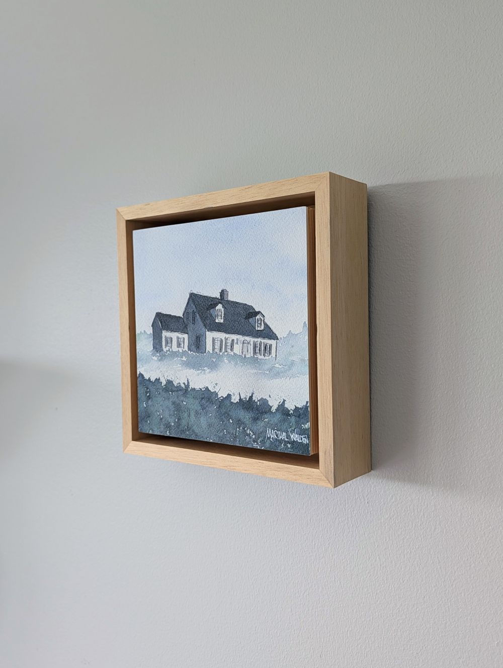 Right side view of Witness, a minimalist monochrome watercolor study of a coastal home, isolated within a deep natural maple float mount frame on a neutral wall.