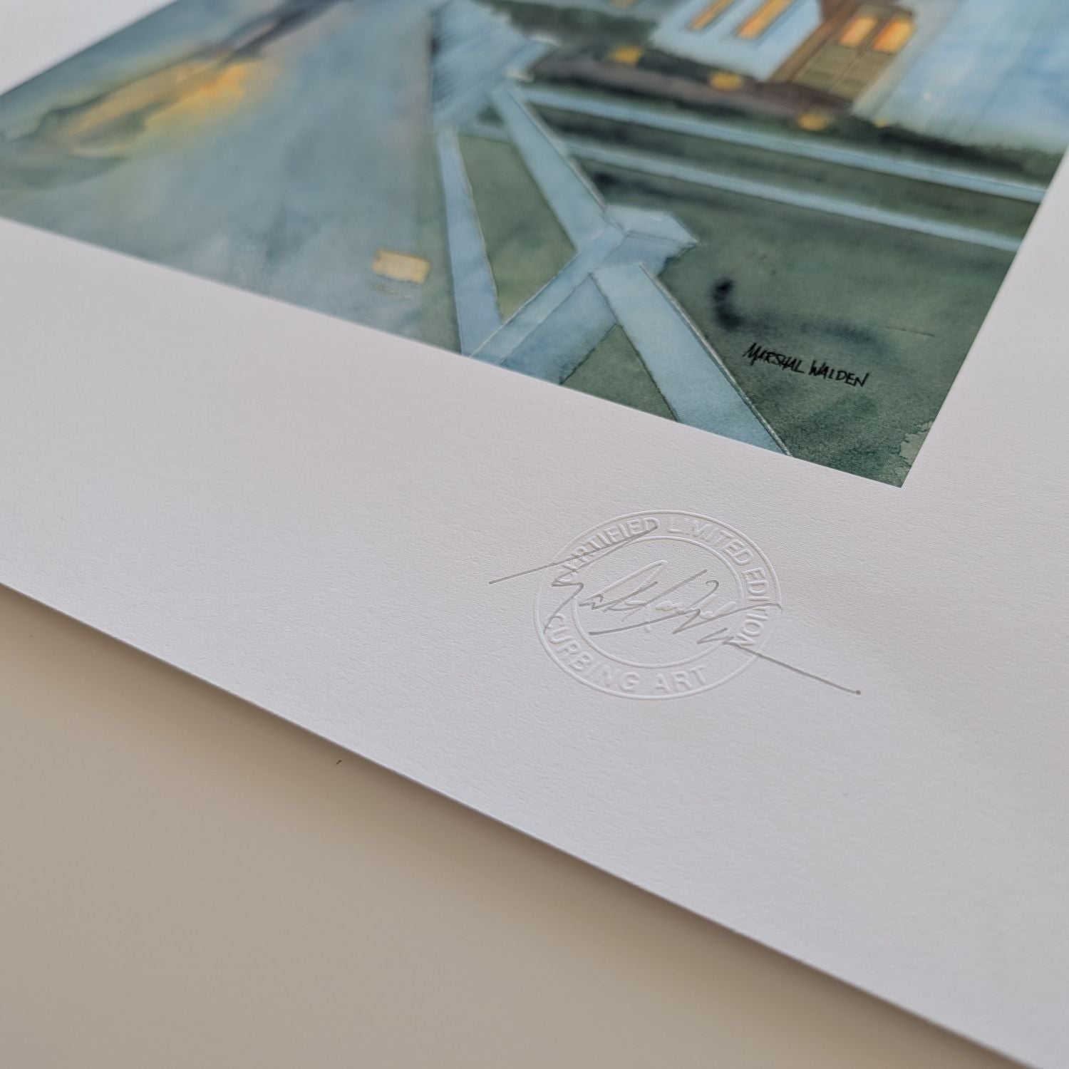 A macro photograph showing the lower corner details of the limited edition fine art print "Stroll In Rain." The focus is on artist Marshal Walden's signature written in graphite pencil next to the raised, circular official "Curbing Art" studio embossing seal pressed into the surface. The lighting and close perspective emphasize the deep texture, tooth, and substantial thickness of the heavy archival paper stock.