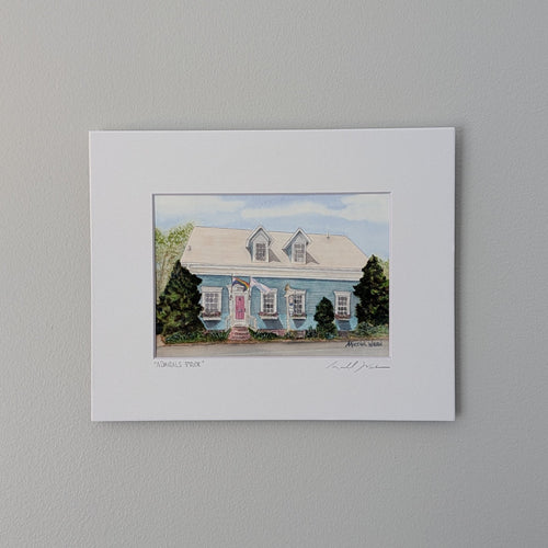 signed by PAAM member artist Marshal Walden. The artwork depicts the historic Admiral's Landing Inn in Provincetown on a bright sunny day, showcasing its teal blue exterior, pink front door, and both the LGBTQ+ rainbow and transgender flags flying out front. The piece is presented in a crisp white mat and centered against a neutral beige wall.
