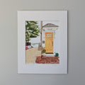 A professional fine art watercolor print titled "The Turn - Yellow Door", hand-titled and signed by PAAM member artist Marshal Walden on the matting. The painting depicts a vibrant yellow door of a coastal home in Provincetown, with a sandy path and colorful kayaks leading toward the harbor under the shade of a large tree. The artwork is presented in a crisp white mat and centered against a neutral beige wall.
