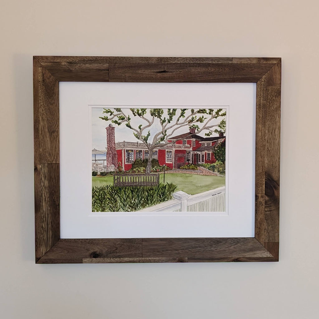 A framed original watercolor painting of The Red Inn in Provincetown, housed in a natural wood frame with a double white mat.