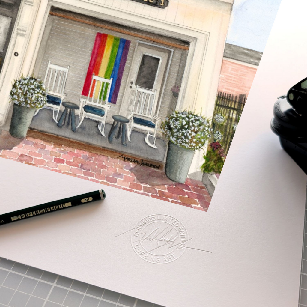 A detailed close-up photograph of the lower corner of the limited edition fine art print "Firehouse Pride." The focus is on the raised, circular "Curbing Art" studio embossing seal pressed into the surface of the paper. Resting beside the seal are the graphite pencil used for signing and numbering, and the metal hand-embossing tool. The texture of the heavy archival fine art paper is clearly visible.
