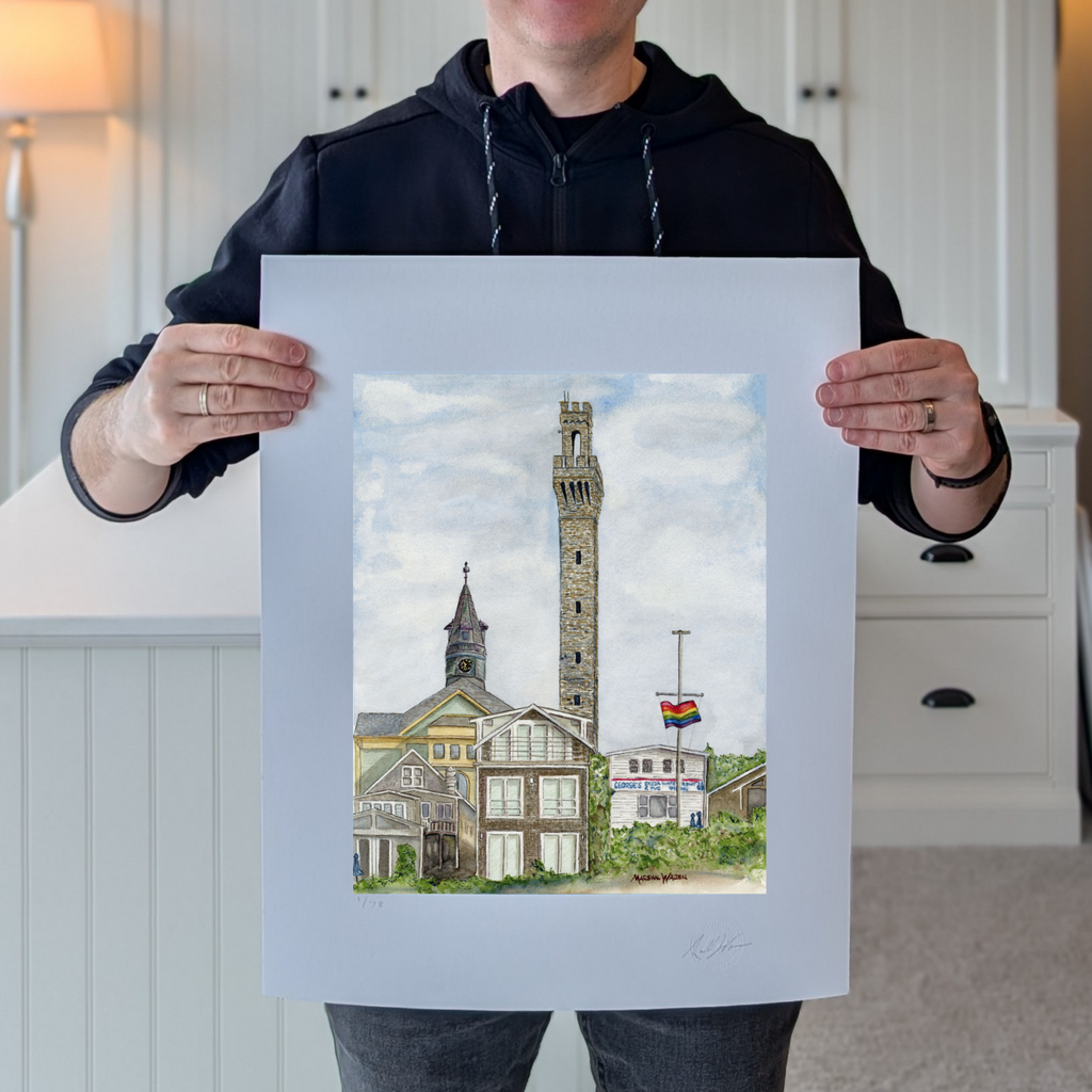 A photograph of artist Marshal Walden holding the large, 16x20 inch limited edition fine art print "Monumental Pride." The image demonstrates the scale of the artwork relative to the artist and highlights the detailed watercolor texture of the Provincetown skyline and the extra-wide crisp white borders. These borders allow for versatile framing, either presented without a mat for a modern look or matted to a standard 11x14 opening for a traditional presentation.
