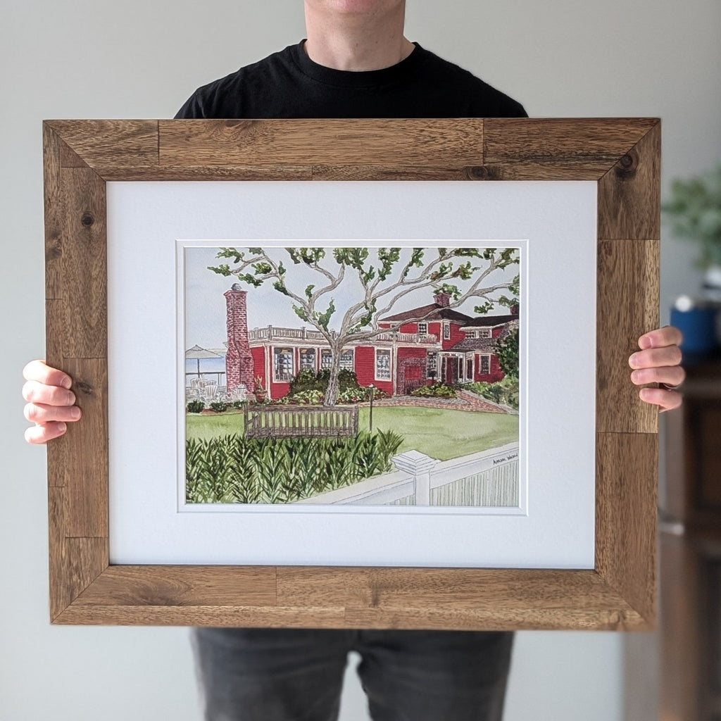 Artist Marshal Walden holding a framed watercolor original of "The Red Inn" in a natural wood frame, demonstrating its size against his body.