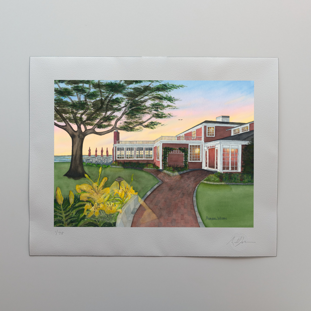 A photograph of a 16x20 limited edition fine art print titled "Red Inn Summer Glow" by PAAM member artist Marshal Walden, resting flat on an off-white tabletop. The artwork is a meditative painting of Provincetown's historic Red Inn, bathed in warm, golden summer sunset light creating long shadows, with visual noise curbed to focus on the architecture. The bottom white border features the artist's hand-penciled signature, the edition numbering "x/78", and a raised Curbing Art embossed seal.
