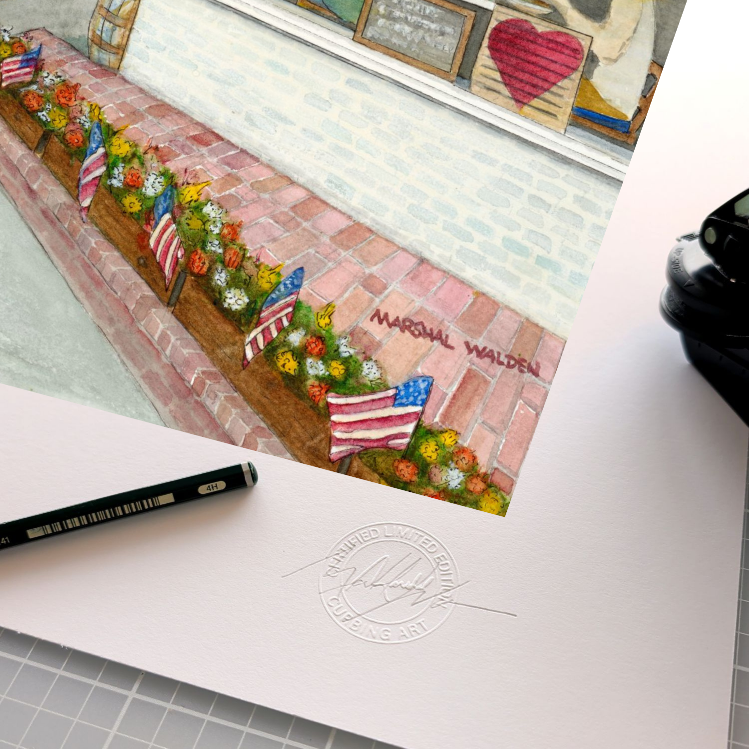 A detailed close-up photograph showing the authentication tools resting on the wide white border of the limited edition fine art print "Window With A View." The focus is on the official, raised circular "Curbing Art" studio embossing seal pressed into the surface of the textured fine art paper. Lying next to the seal are the artist's graphite pencil used for signing and numbering, and the metal hand-embossing tool used to create the seal. A portion of the watercolor artwork of Liz's Cafe is visible at the e